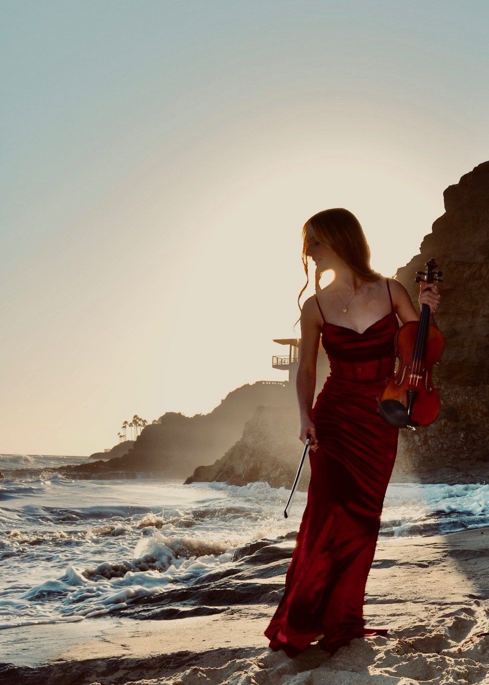 Hannah in a burgundy gown on the shore at sunset, violin in hand